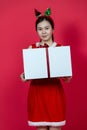 Mockup Image of an Asian Woman Presenting a Big Gift Box With Christmas Attire on a Red Background Royalty Free Stock Photo