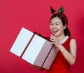 Mockup Image of an Asian Woman Presenting a Big Gift Box With Christmas Attire on a Red Background Royalty Free Stock Photo