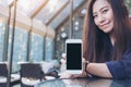 Mockup image of a beautiful asian woman holding and showing white mobile phone with blank black screen Royalty Free Stock Photo