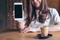 A beautiful woman holding and showing white mobile phone with blank black desktop screen with coffee cup on wooden table Royalty Free Stock Photo
