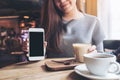 A beautiful woman holding and showing white mobile phone with blank black desktop screen with coffee cups on vintage wooden table Royalty Free Stock Photo