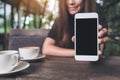 Mockup image of a beautiful woman holding and showing white mobile phone with blank black screen with coffee cups Royalty Free Stock Photo