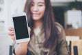 A beautiful woman holding and showing white mobile phone with blank black screen with smiley face in vintage wooden cafe Royalty Free Stock Photo