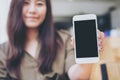 A beautiful woman holding and showing white mobile phone with blank black screen with smiley face in vintage wooden cafe Royalty Free Stock Photo