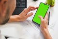 Mockup image, man hand holding blank green screen mobile smart phone, working on laptop Royalty Free Stock Photo