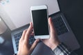 Mockup image of business woman holding mobile phone with blank black screen while using laptop Royalty Free Stock Photo