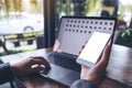 Mockup image of business woman holding mobile phone with blank white screen while using laptop Royalty Free Stock Photo