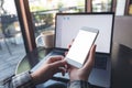 Mockup image of business woman holding mobile phone with blank white screen while using laptop Royalty Free Stock Photo