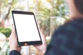 Mockup image of business woman`s hands holding black tablet pc with blank desktop white screen in cafe and green nature Royalty Free Stock Photo