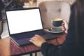 Mockup image of a businesswoman using laptop with blank white desktop screen while drinking hot coffee on wooden table Royalty Free Stock Photo