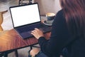 Mockup image of a businesswoman using laptop with blank white desktop screen while drinking hot coffee on wooden table