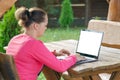 Mockup image, girl uses laptop with blank white screen on old wooden table in gazebo outdoors