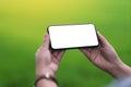 A hand holding black mobile phone with blank desktop screen with blur green nature background Royalty Free Stock Photo