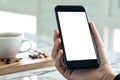 Mockup image of hand holding black mobile phone with blank white desktop screen with coffee cup Royalty Free Stock Photo