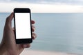 A hand holding black mobile phone with blank white screen with blue sky , white beach and the sea in background Royalty Free Stock Photo