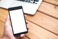 Mockup image of hand holding black mobile phone with blank white screen and silver color laptop on vintage wooden table Royalty Free Stock Photo