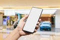 Mockup image of hand holding blank screen mobile smart phone with blurred background of new cars display in showroom, buying new