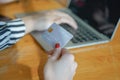 Mockup image of a hand holding credit card when using laptop making online payment with her friend on wooden table. Royalty Free Stock Photo