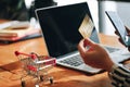 Mockup image of a hand holding credit card when using laptop making online payment with and Ã Â¸Â«hopping carton wooden table.