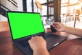 Mockup image of a hand holding credit cards while using and typing on laptop with blank green screen and coffee cup Royalty Free Stock Photo