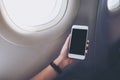 A hand holding and looking at white smart phone with black screen next to an airplane window with clouds and sky background Royalty Free Stock Photo