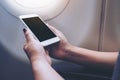 Mockup image of a hand holding and looking at white smart phone with blank desktop screen next to an airplane window Royalty Free Stock Photo