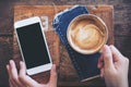Mockup image of a hand holding mobile phone with blank black screen and coffee cup Royalty Free Stock Photo