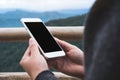 A hand holding and showing white smart phone with blank black desktop screen in outdoor with blur green mountains background Royalty Free Stock Photo