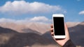 Mockup image of a hand holding and using white mobile phone with blank black screen while standing in front of mountains Royalty Free Stock Photo