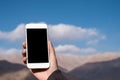 Mockup image of a hand holding and using white mobile phone with blank black screen while standing in front of mountains Royalty Free Stock Photo