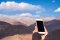 Mockup image of a hand holding and using white mobile phone with blank black screen while standing in front of mountains Royalty Free Stock Photo