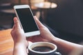 Mockup image of hand holding white mobile phone with blank black desktop screen with coffee cup on wooden table Royalty Free Stock Photo