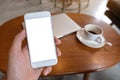 Hand holding white mobile phone with blank desktop screen with coffee cup and laptop on table Royalty Free Stock Photo