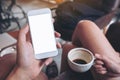 A hand holding white mobile phone with blank desktop screen and a woman holding black coffee cup while sitting in cafe Royalty Free Stock Photo