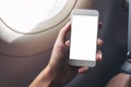 A hand holding a white smart phone with blank desktop screen next to an airplane window Royalty Free Stock Photo