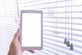 Mockup image of hand holds a tablet by a window where light have passes through the open blinds