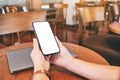 Hands holding black mobile phone with blank desktop screen with laptop computer on the table Royalty Free Stock Photo