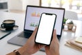 Hands holding a black mobile phone with blank screen while using laptop computer in office Royalty Free Stock Photo