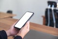 Hands holding black mobile phone with blank white screen with laptop on wooden table Royalty Free Stock Photo