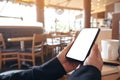 Hands holding black mobile phone with blank white screen horizontally with coffee cup on wooden table in vintage Royalty Free Stock Photo