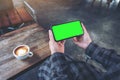 Hands holding black mobile phone with blank white screen horizontally with coffee cup on wooden table in vintage Royalty Free Stock Photo