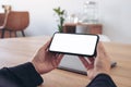 Hands holding black mobile phone with blank white screen horizontally for watching with laptop on table in office Royalty Free Stock Photo