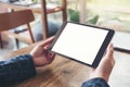 Hands holding black tablet pc with blank white desktop screen and laptop on wooden table in cafe Royalty Free Stock Photo