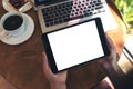 Mockup image of hands holding black tablet pc with blank white screen , laptop , coffee cup and cake on wooden table Royalty Free Stock Photo