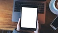 Mockup image of hands holding black tablet pc with white blank screen and laptop , coffee cup on wooden table background Royalty Free Stock Photo