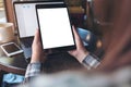 Mockup image of hands holding black tablet pc with white blank screen , laptop , smartphone and coffee cup on table Royalty Free Stock Photo