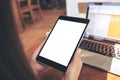 Mockup image of hands holding black tablet pc with white blank screen and laptop on wooden table background Royalty Free Stock Photo