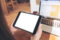 Mockup image of hands holding black tablet pc with white blank screen and laptop on wooden table background Royalty Free Stock Photo