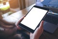 Mockup image of hands holding black tablet pc with white blank screen and laptop on wooden table background Royalty Free Stock Photo