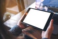 Mockup image of hands holding black tablet pc with white blank screen and laptop on wooden table background Royalty Free Stock Photo